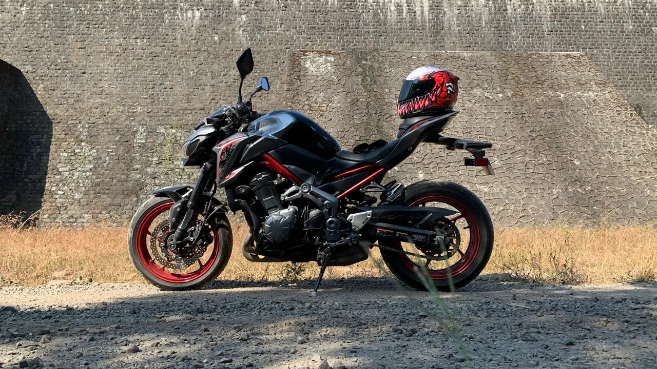 The black and red Kawasaki Z900 against a stone fort wall, a Venom-graphic helmet resting on the tail